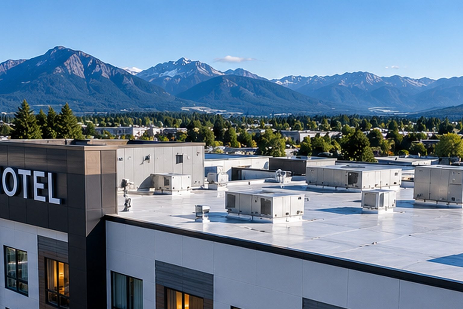 Hotel building with a flat roof and rooftop units, mountains in the distance